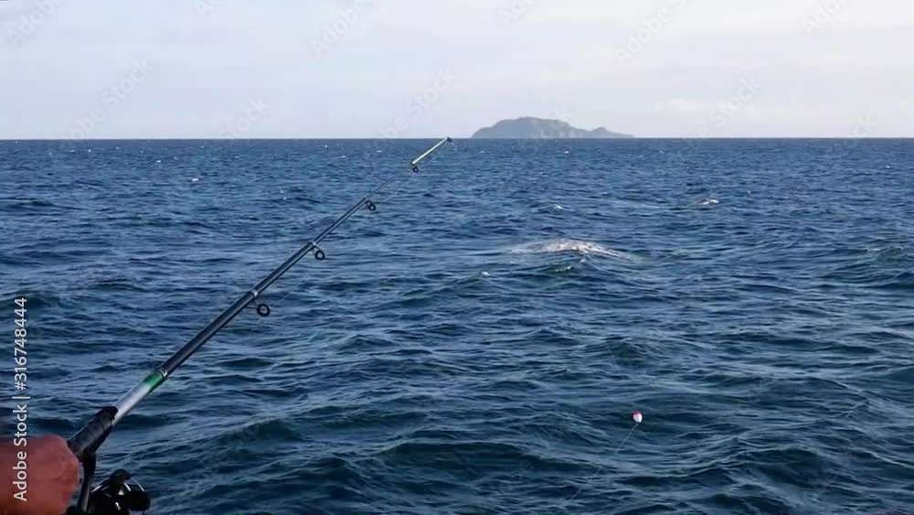 A man is fishing on the ocean. An island is visible on the horizon. A man is fishing on the ocean. An island is visible on the horizon.