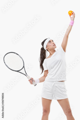 Young female tennis player holding orange and racket against white background © moodboard