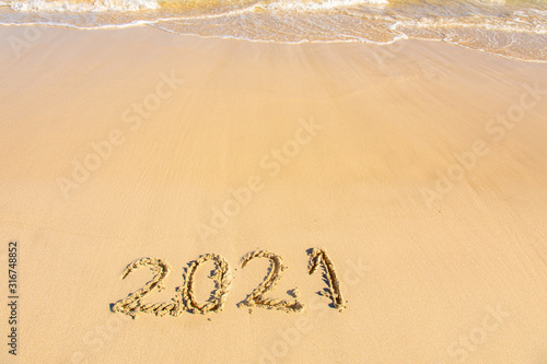 New Year 2021 is coming - inscription 2021 on a beach sand, the wave is starting to cover the digits - Summer beach holiday 2021 season golden sand - old year - message handwritten - empty copy space