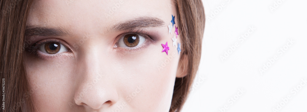 Fototapeta premium Cropped image of beautiful young woman with stars on her face against white background