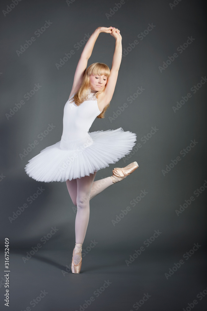 Young woman in white tutu performing ballet over grey background