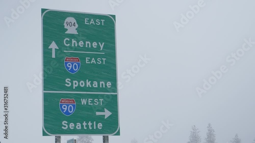 CLOSE UP: Green traffic sign directs traffic around the state of Washington during a snowstorm. Highway traffic sign weathers a blizzard engulfing the state of Washington. Arrows pointing to US cities photo