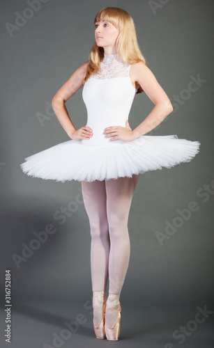 Young female ballet dancer in wearing tutu tiptoeing over grey background