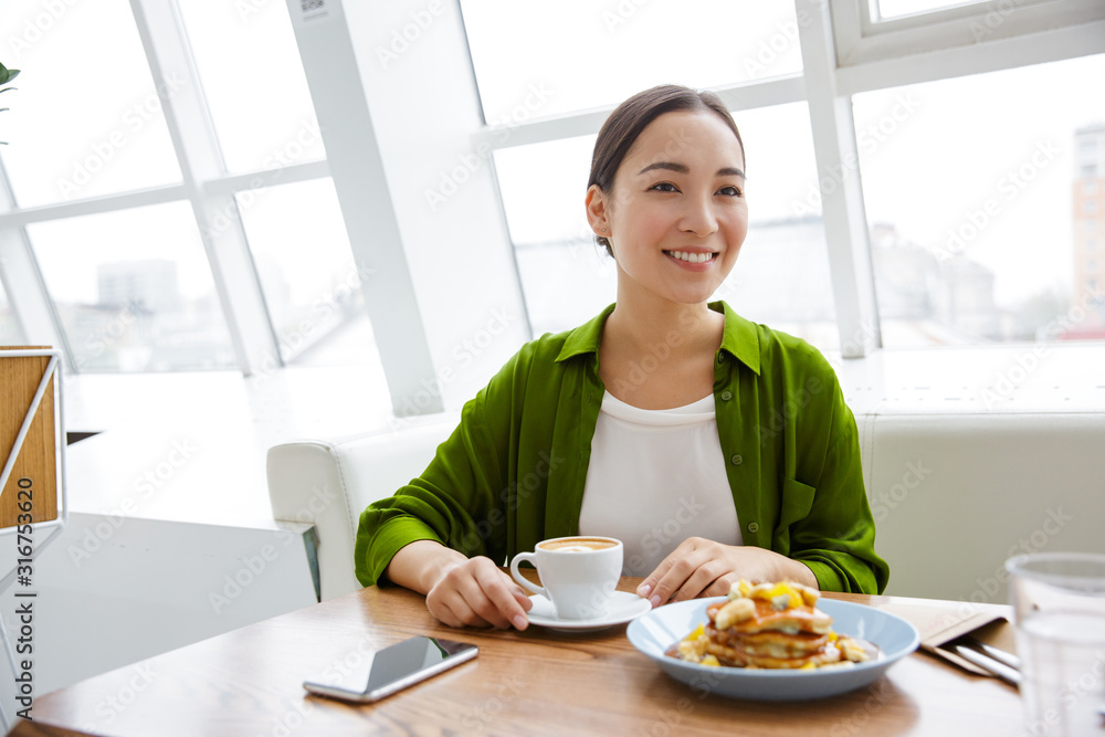 Smiling asian woman having pancakes for breakfast