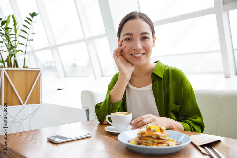 Smiling asian woman having pancakes for breakfast