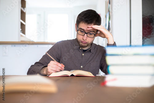 Learning and studying concept: Young exhaust and unhappy male student is learning at home, stack of books