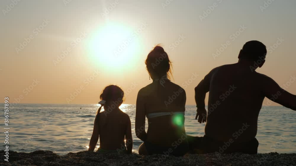 Parents with their child enjoy the sunset by the sea or ocean shore. Family is relaxing on the beach at sundown. Happy childhood and parenthood concept. Parents with their child enjoy the sunset by the sea or ocean shore. Family is relaxing on the beach at sundown. Happy childhood and parenthood concept.