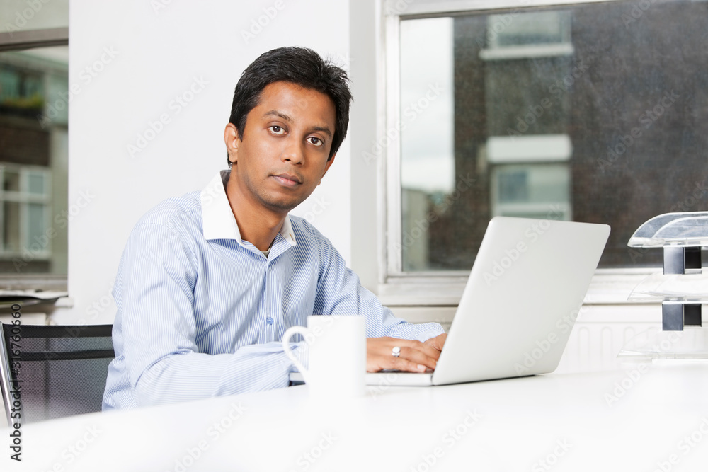 Portrait of young businessman using laptop at desk in office Portrait of young businessman using laptop at desk in office