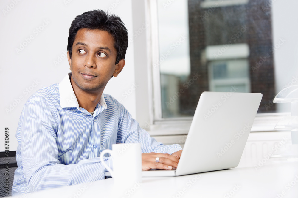 Young businessman with laptop sitting at desk in office Young businessman with laptop sitting at desk in office