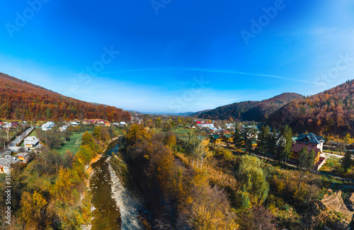 Aerial panoramic view of the village of Sheshory, surrounded by the Carpathian mountains. Buildings and infrastructure. The nature of Ukraine. Sunny autumn day. Huk waterfall on the Pistynka River. photo