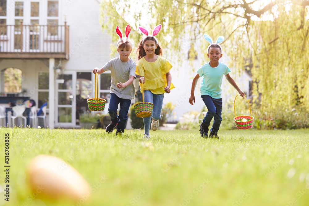Fototapeta premium Group Of Children Wearing Bunny Ears Running On Easter Egg Hunt In Garden