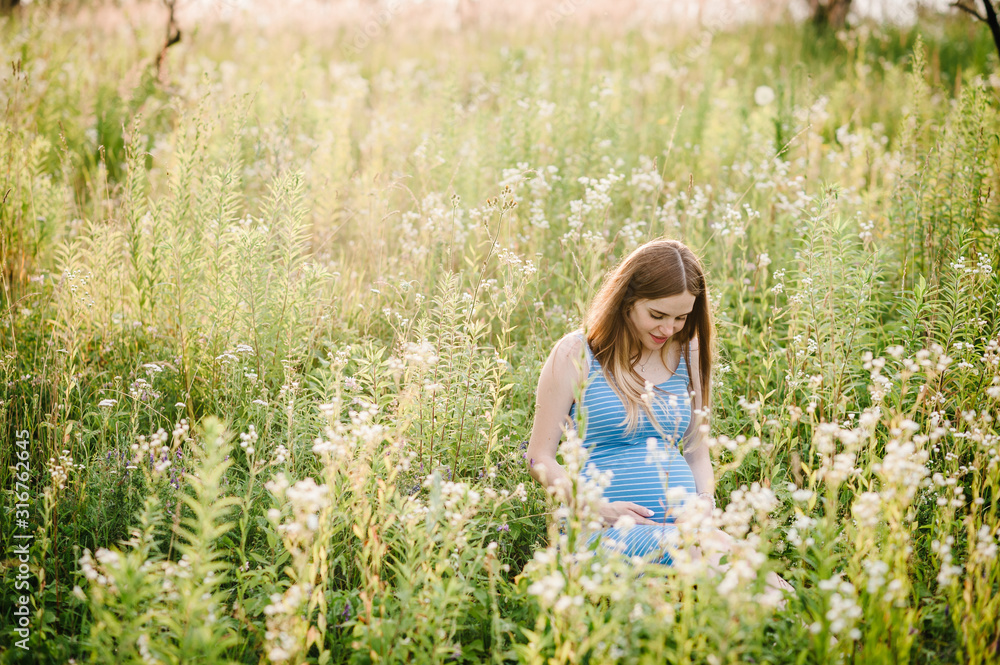 Pregnant happy girl sits and hold hands on stomach, sitting on background green grass in field in the outdoor. Close up. upper half. Look down at the stomach Pregnant happy girl sits and hold hands on stomach, sitting on background green grass in field in the outdoor. Close up. upper half. Look down at the stomach