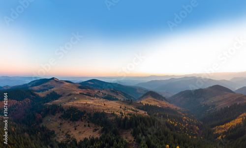 Aerial view of the Carpathian mountains in autumn. Pine forest, houses on the peaks, yellow fields and trees. Mountain meadow. sunset, Ukraine, Europe