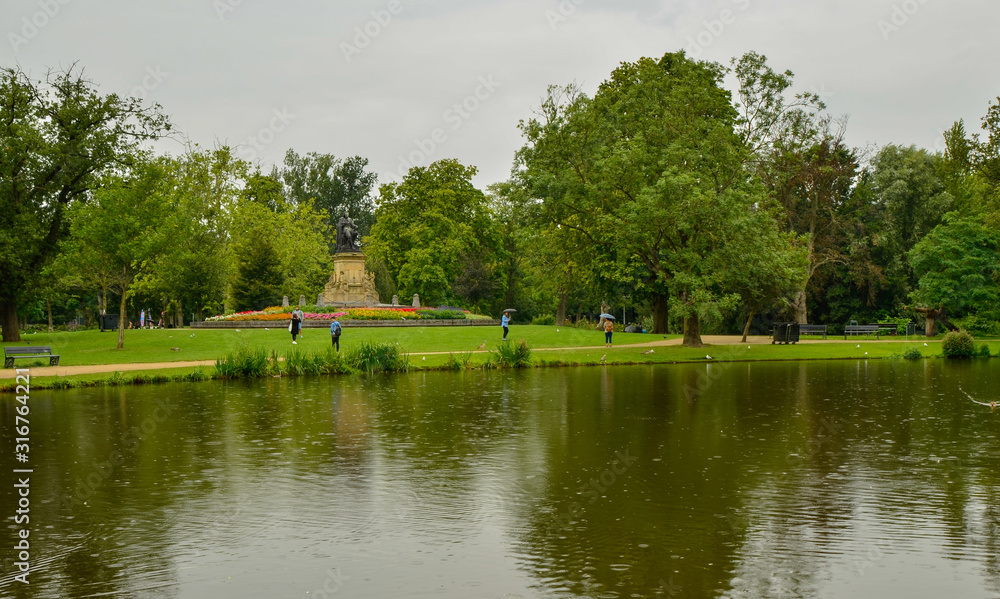 Amsterdam, Holland, August 2019. The Vondelpark: the large park in the heart of the city. On a rainy day, view of one of the lakes: people stroll with an umbrella enjoying the beauty of the place.