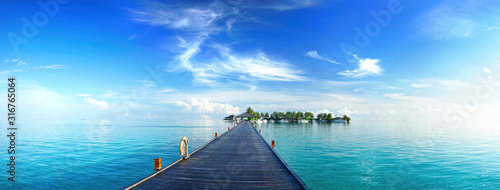 Beautiful tropical landscape background, concept for summer travel and vacation. Wooden pier to an island in ocean against blue sky with white clouds, panoramic view. © Laura Pashkevich