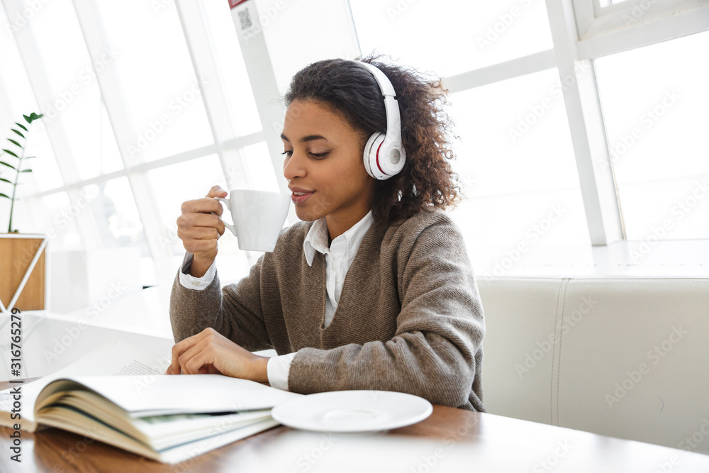 Obraz premium Portrait of young african american woman reading book on sofa in cafe