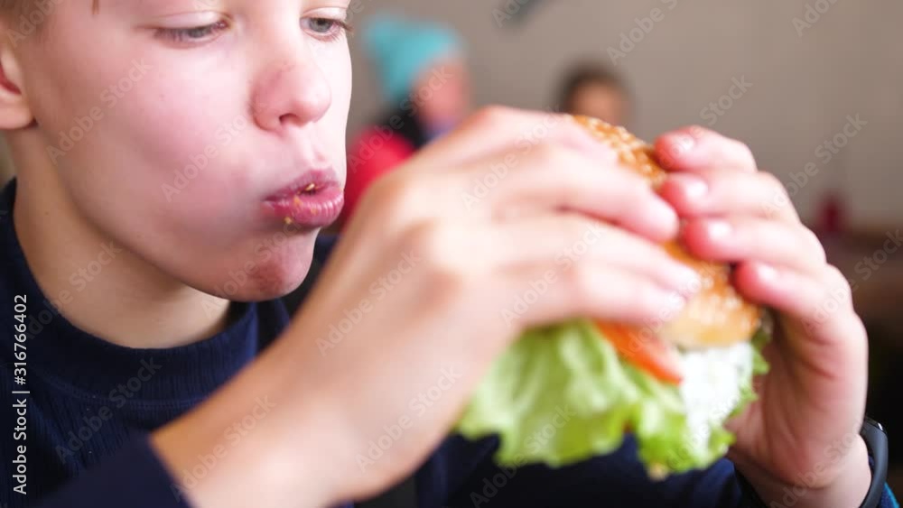 A child eats a bun with a cutlet and cheese in a fast food restaurant A child eats a bun with a cutlet and cheese in a fast food restaurant
