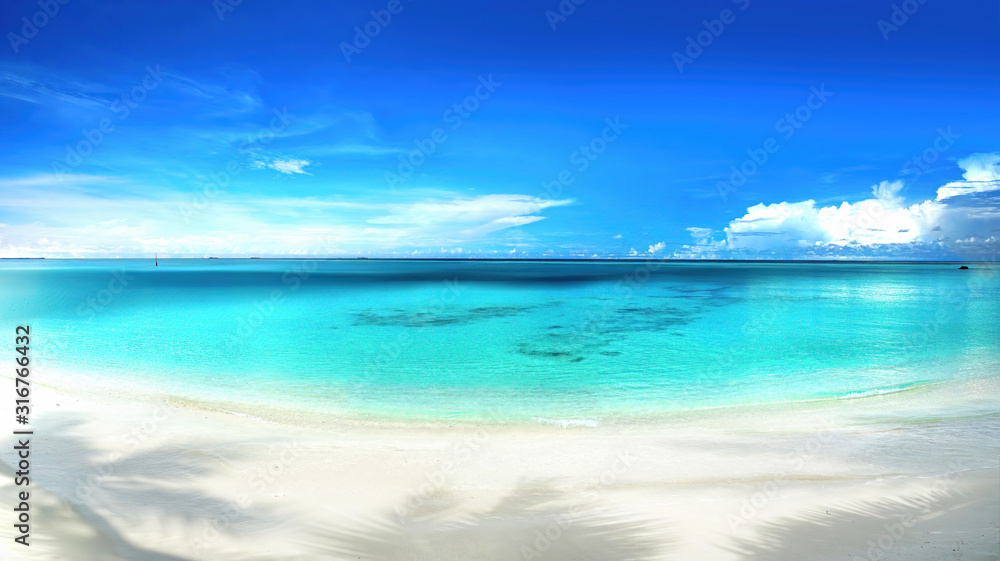 Beautiful beach with white sand, shadows from leaves of palm trees, turquoise ocean water and blue sky with clouds in sunny day. Panoramic view. Natural background for summer vacation.