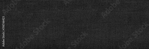 Panoramic close-up texture of natural weave cloth in dark and black color. Fabric texture of natural cotton or linen textile material. Black fabric wide background.