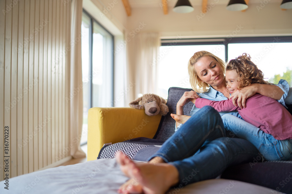 Fototapeta premium A cute small girl with mother on sofa indoors at home, resting.
