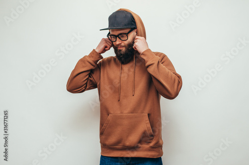 Handsome hipster guy with beard wearing brown blank hoodie or hoody and black cap with space for your logo or design on white background. Mockup for print