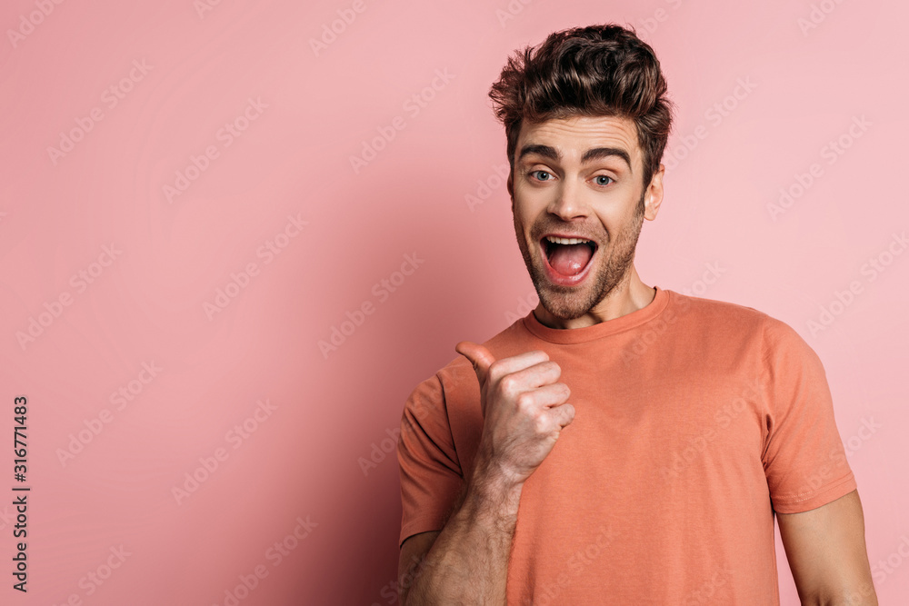 excited man pointing with thumb while looking at camera on pink background excited man pointing with thumb while looking at camera on pink background
