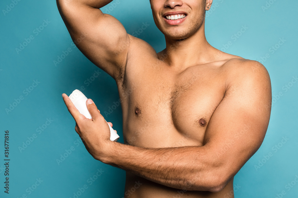 Beauty portrait of half naked handsome young man with beautiful torso dressed in towel using deodorant smiling isolated over blue background