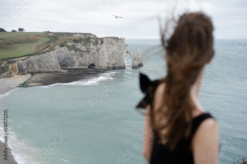 A girl stands on a cliff of the coast of France etretat and admires the sea and her hair develops romantically in the wind.