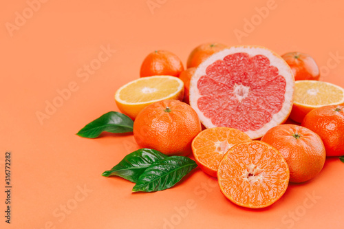 Fresh ripe mandarins  grapefruit and oranges with green leaves on orange background.