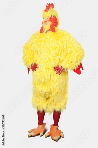 Young man in chicken suit standing with hands on hips against gray background photo