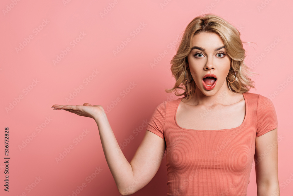surprised girl pointing with hand while looking at camera on pink background surprised girl pointing with hand while looking at camera on pink background