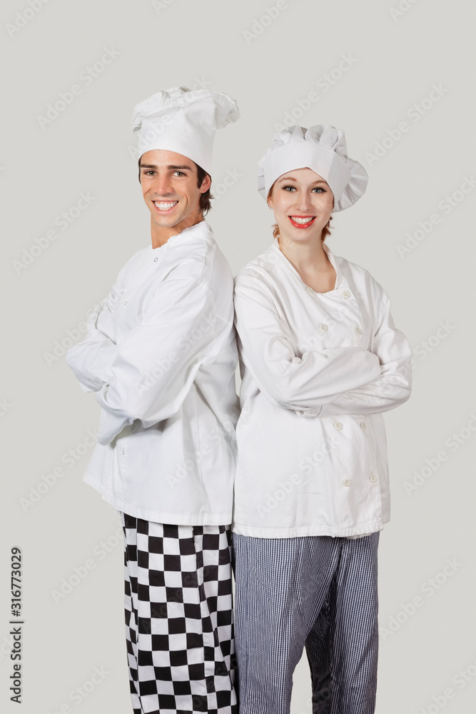 Portrait of young man and woman in chef's uniform with arms crossed against gray background