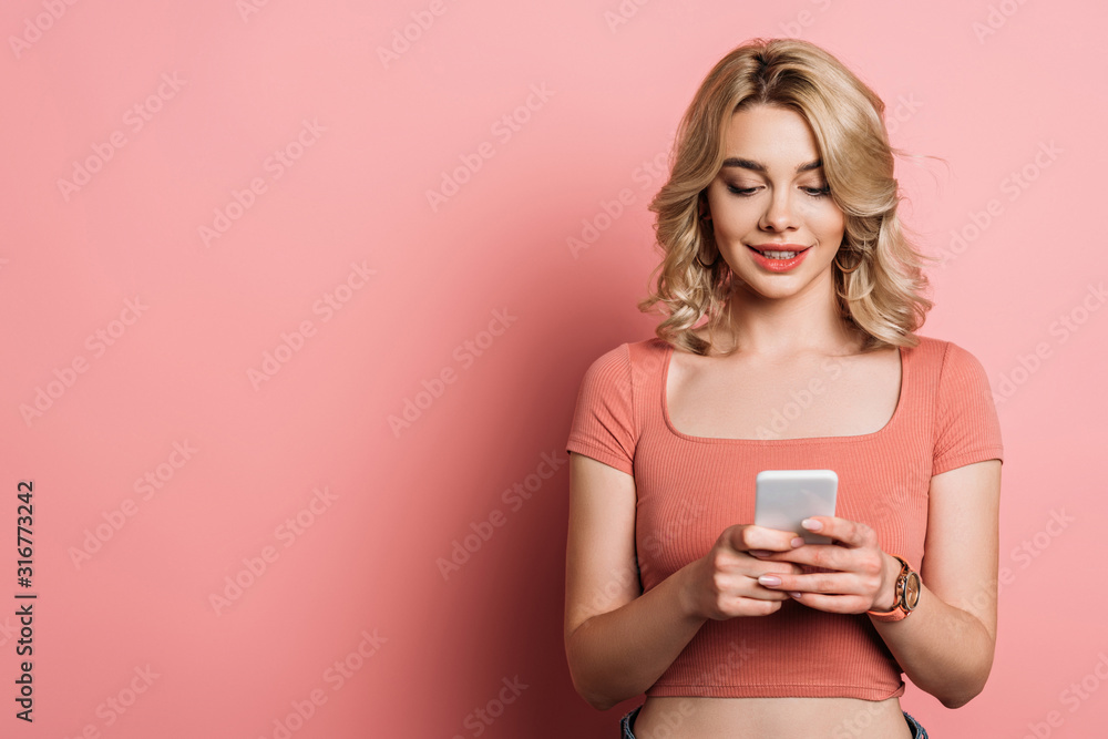 beautiful, smiling girl chatting on smartphone on pink background