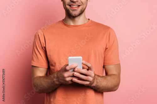 cropped view of smiling man using smartphone on pink background © LIGHTFIELD STUDIOS