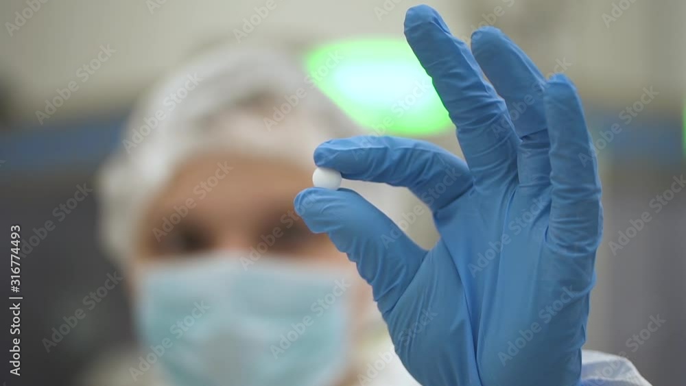 Woman employee holding white pill in hand during working day in pharmaceutical company. Closeup view of caucasian female worker is showing tablet while standing in interior of pharma chemical plant Woman employee holding white pill in hand during working day in pharmaceutical company. Closeup view of caucasian female worker is showing tablet while standing in interior of pharma chemical plant