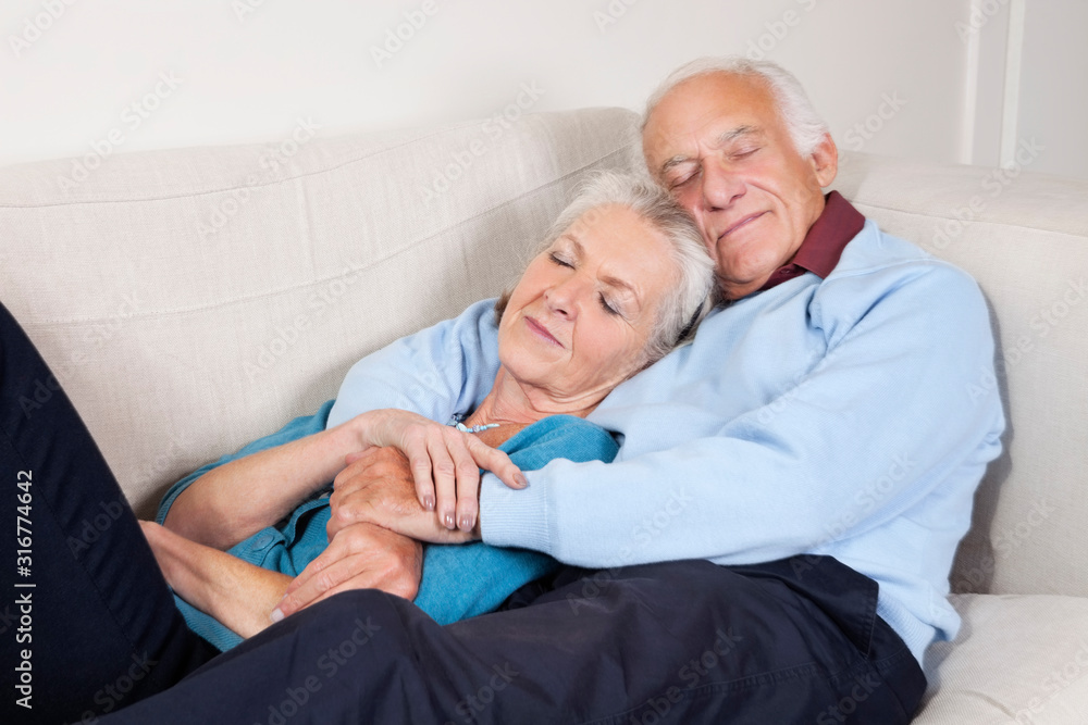 Romantic senior couple with arms around relaxing on sofa at home Romantic senior couple with arms around relaxing on sofa at home