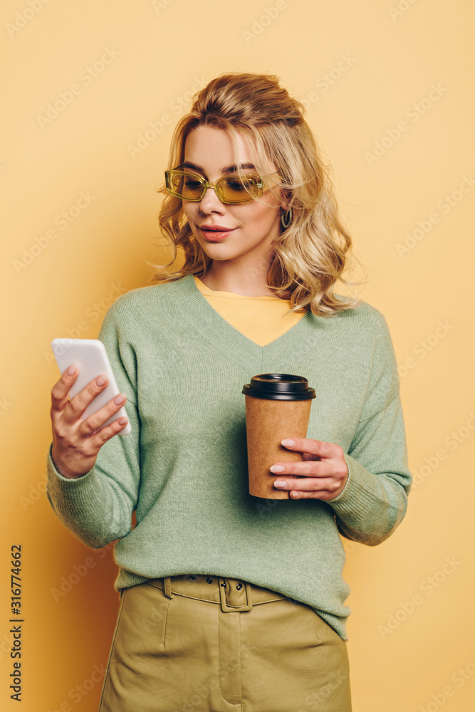 stylish, smiling girl holding coffee to go while chatting on smartphone on yellow background stylish, smiling girl holding coffee to go while chatting on smartphone on yellow background