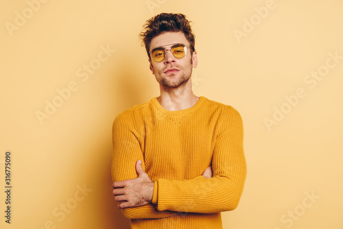 handsome, confident man looking at camera while standing with crossed arms on yellow background © LIGHTFIELD STUDIOS