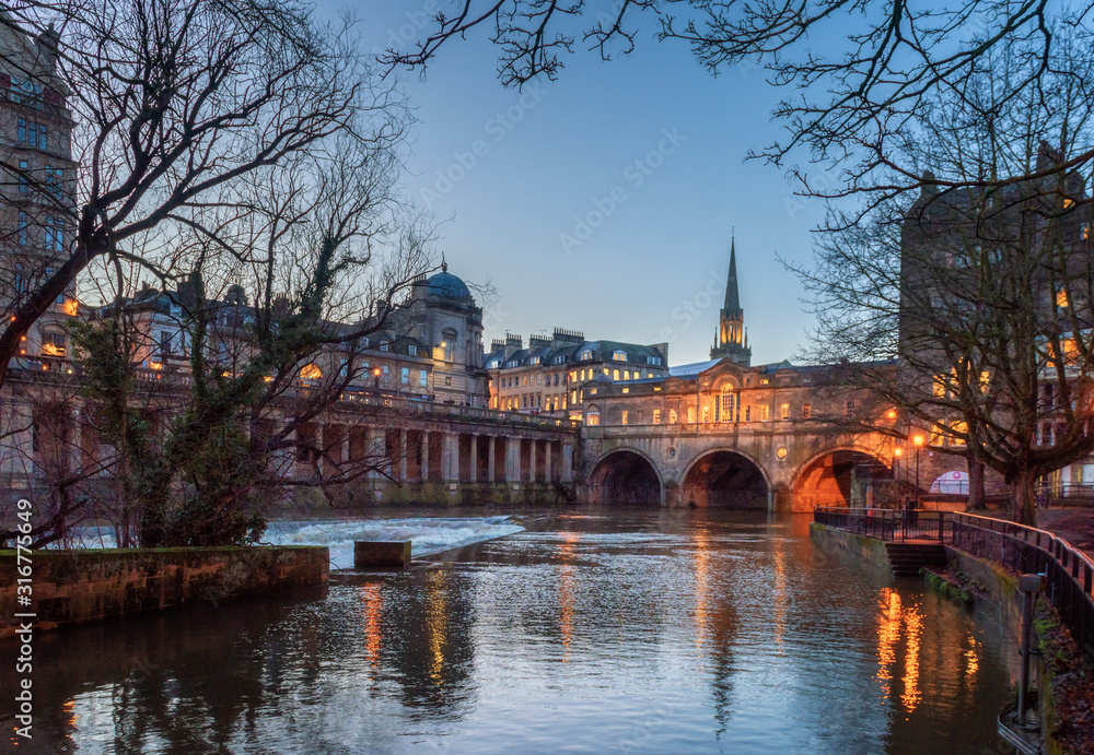 Pulteney Bridge with reflection in Avon river with dry tree foreground during twilight at Bath, UK