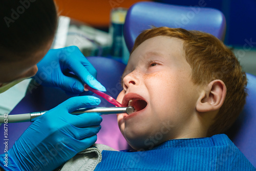 Scared red-haired boy crying at reception at dentist in dental chair