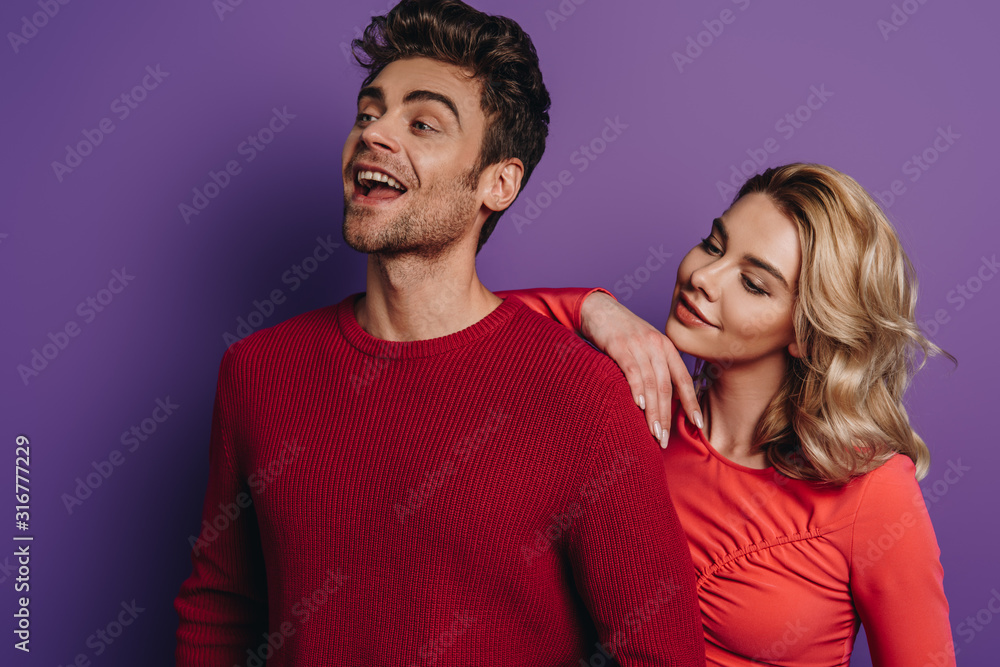 Obraz premium happy girl leaning on shoulder of smiling boyfriend looking away on purple background