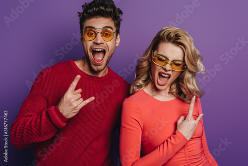 excited man and woman showing rock signs on purple background