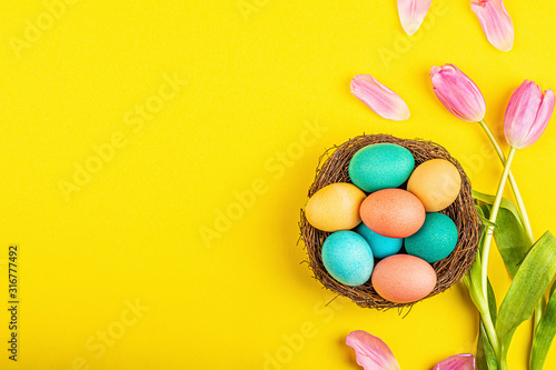 Stylish background with colorful easter eggs isolated on yellow background with pink tulip flowers. Flat lay, top view, mockup, overhead, template