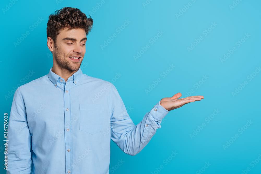 smiling young man looking at open arm on blue background smiling young man looking at open arm on blue background