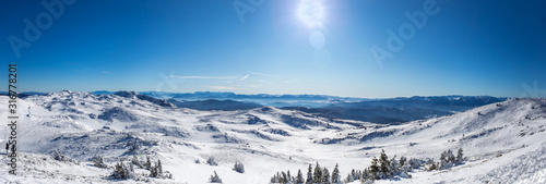 Panoramic shot from the top of the mountain in winter season. Everything is covered in snow and looks beautiful. The day is sunny and the sky is clear and blue.
