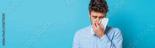 panoramic shot of diseased man sneezing in paper napkin on blue background photo