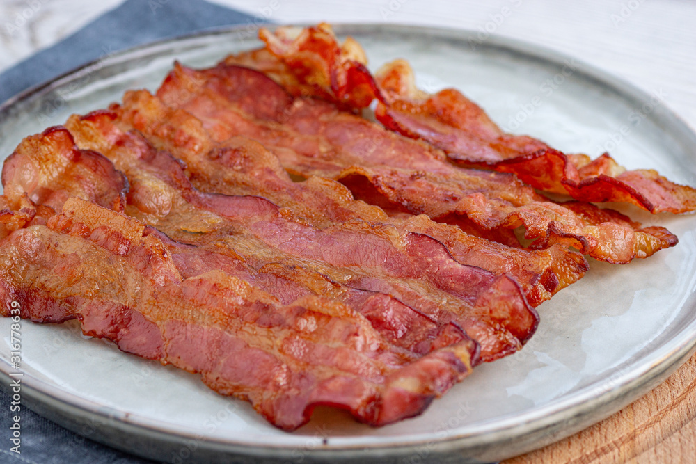 Crispy fried bacon in a cast iron pan on a gray background. Crispy fried bacon in a cast iron pan on a gray background.