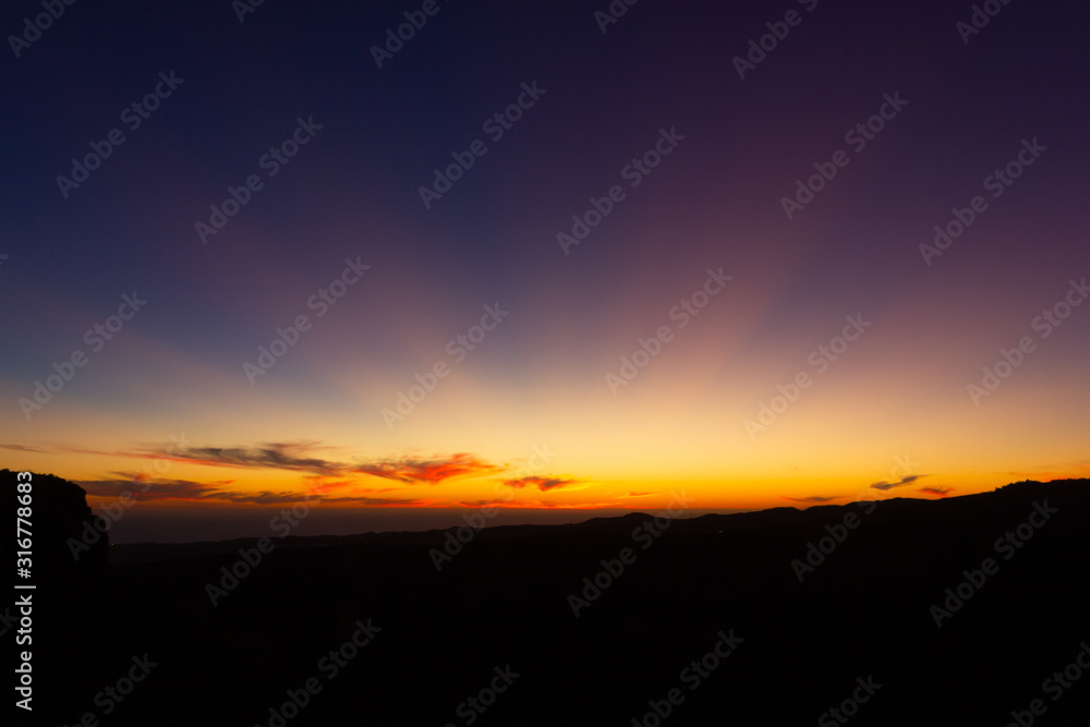 Bright sun rays over blue purple sky at sunset in Gran Canaria, Spain. Colorful twilight in Canary Islands. Natural landscape concept