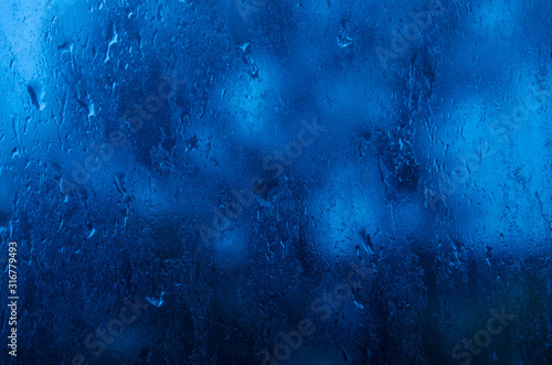 Raindrops on the window glass. Blue twilight light. Rainy weather.