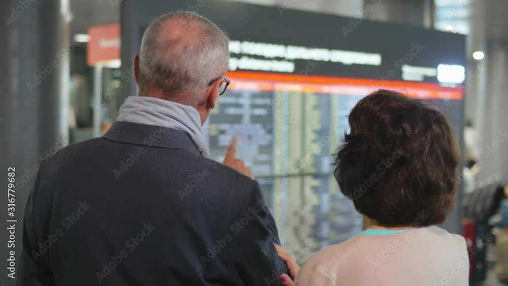 Back view of elderly couple checking flight timetable in international airport Back view of elderly couple checking flight timetable in international airport